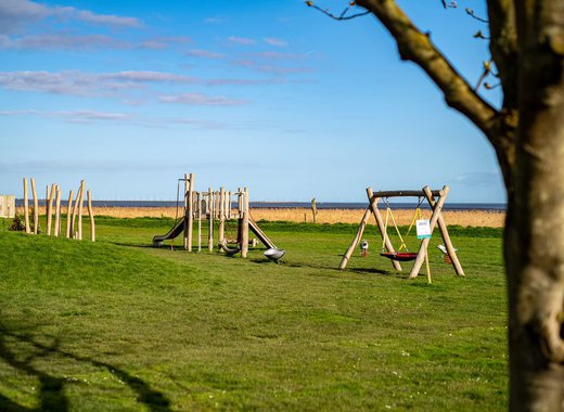 The outdoor adventure playground at our Essex holiday park, Mersea Island, on a sunny day with views of the sea in the background.