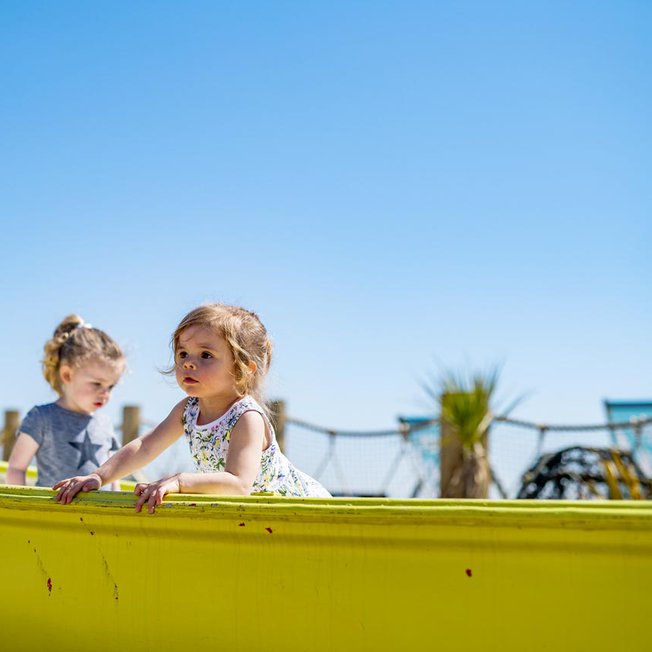 
              A bright and sunny day with two young children playing in a yellow boat at our holiday park in Whitecliff Bay.
              