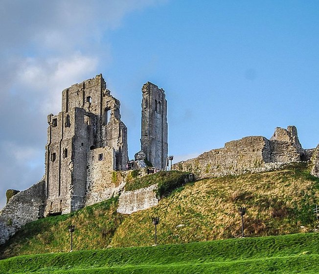 An image of Corfe Castle on a bright day with blue skies.
