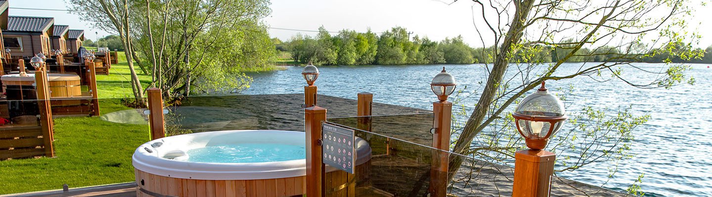 
          The outside of our lodges situated in a holiday park near a lake. There's a hot tub outside.
          