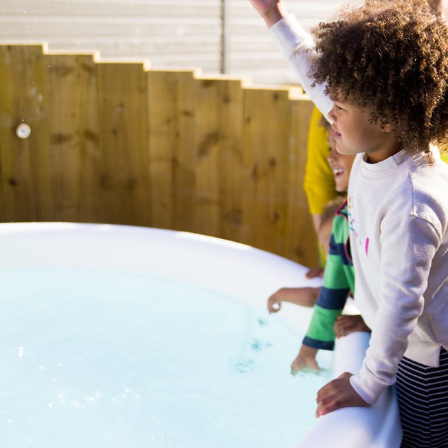 
                Three young children playing outside one of the hot tubs at our Whitecliff Bay holiday park.
                