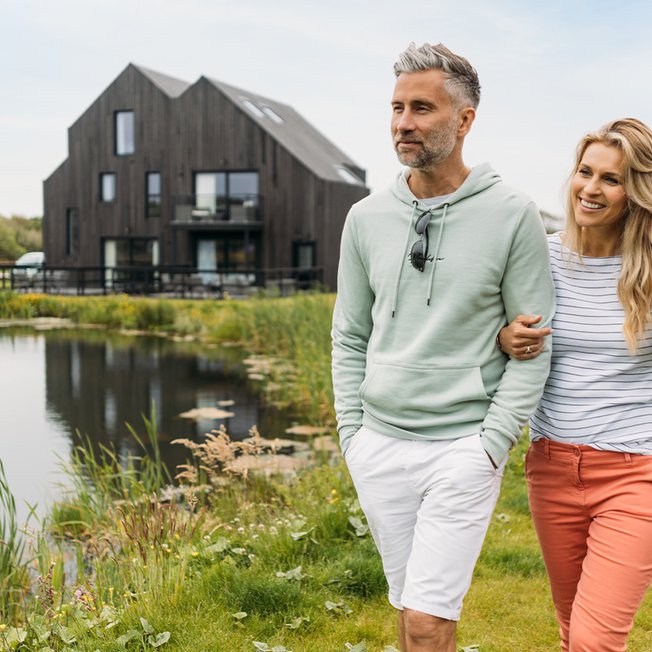 
              A middle-aged couple, link arms as they walk past a lake with one of our barns in the background.
              