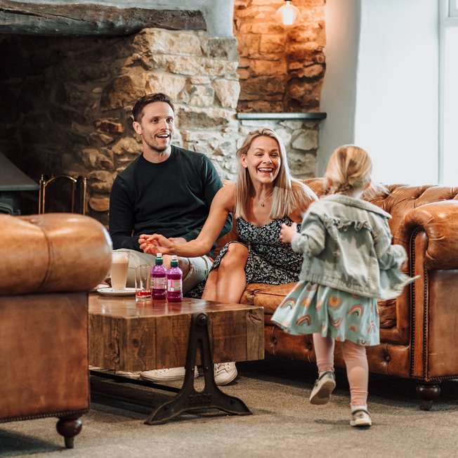 
                A little girl running towards her mum and dad, who are sat on the sofa in one of our on park restaurants.
                