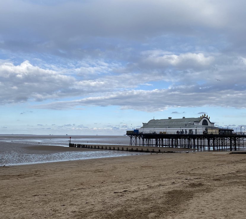 An overcast day looking out at the horizon of Cleethorpes Pearl pier. The beach is sandy and the waves are mostly calm.