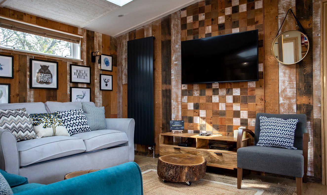 The lounge area in The Knightwood holiday lodge. This lodge has large sofas, a flatscreen TV, and plenty of rustic, woodland décor to enjoy.