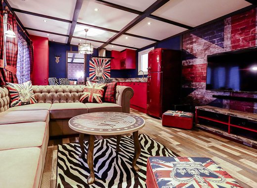 The interior of The Rockstar holiday home. There's a variety of luxurious furniture, each with a British rockstar theme and colour. There's a long, cream sofa, a TV, and a red fridge in the spacious kitchen.