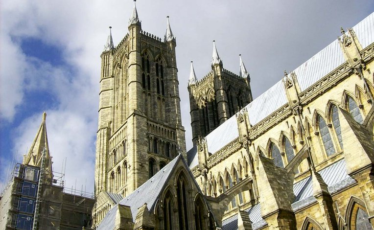 A photo of the Lincoln cathedral taken from below looking up at one of the spires on a cloudy day.