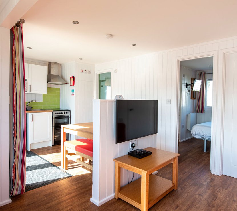The interior of one of our holiday home Chalets. There’s a large TV, double bedroom, and kitchen space. There are bright colours in the holiday home.