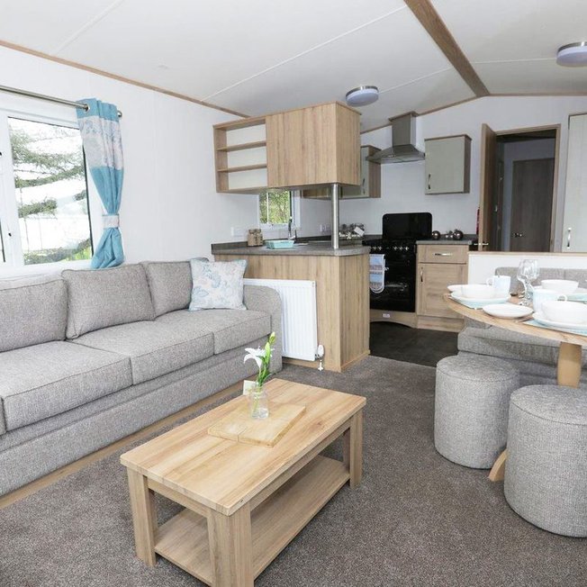 
                Suggested: The interior of one of our luxury caravans. There's a large, grey sofa, a seating area with a table, and a kitchen space with several appliances.
                