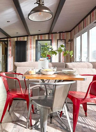 An image of the interior of one of our holiday lodges. There's wooden panneling, a cream fabric sofa and red metal dining chairs around a wooden table.