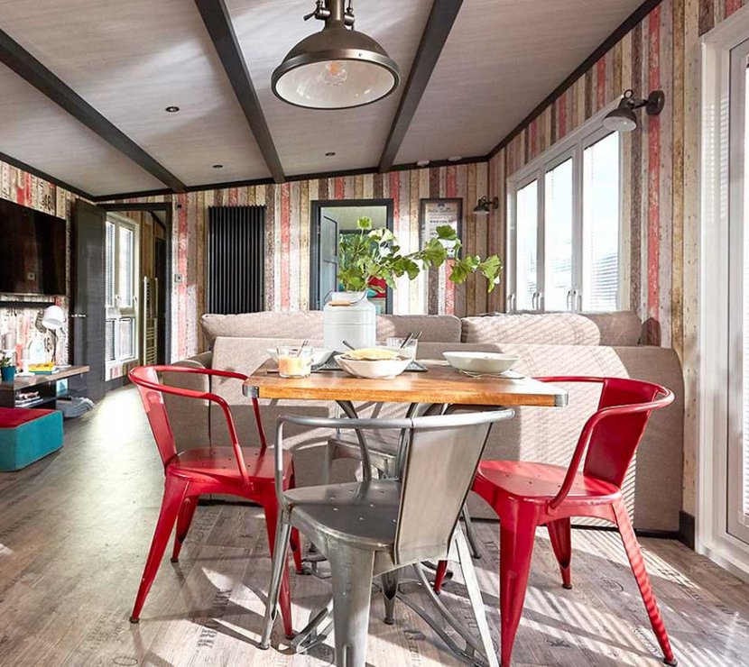 An image of the interior of one of our holiday lodges. There's wooden panneling, a cream fabric sofa and red metal dining chairs around a wooden table.