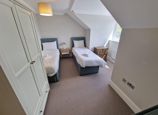 A twin room in one of our cottages. The room contains two single beds, a wooden wardrobe, a chest of drawers and a bedside table with a lamp.