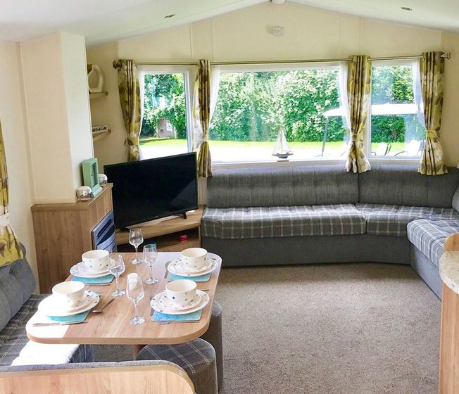The interior of one of our Superior caravan holiday homes. There’s a large sofa, flatscreen TV, and a comfortable dining area.