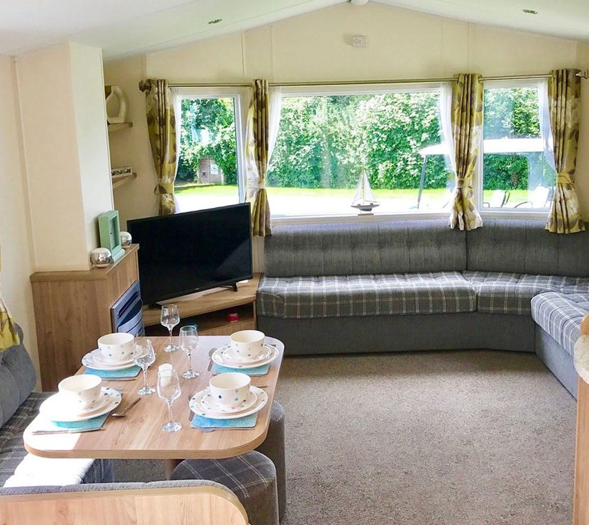 The interior of one of our Superior caravan holiday homes. There’s a large sofa, flatscreen TV, and a comfortable dining area.