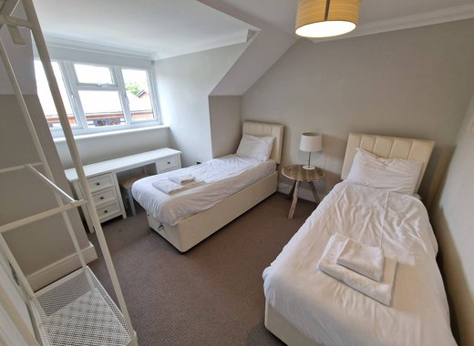 A twin room in one of our cottages. Within the room are two single beds, clothes hanging area, a bedside table with a lamp and a vanity unit below the window.