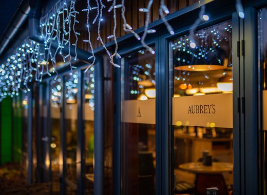 A nighttime photo of a building with hanging blue-white fairy lights above some windows. There's a yellow sign which says, ''Aubery's''