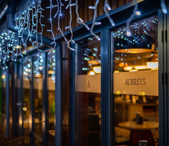 A nighttime photo of a building with hanging blue-white fairy lights above some windows. There's a yellow sign which says, ''Aubery's''