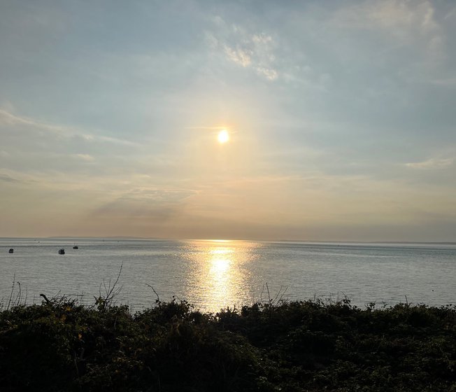 A sunset on the beach in The Bay Colwell. The sun is drifting down and the light is spread across the sea view. There are four boats in the near distance, and another four much farther out.