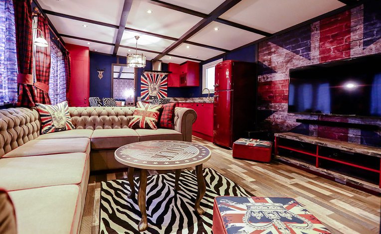 The interior of The Rockstar holiday home. There's a variety of luxurious furniture, each with a British rockstar theme and colour. There's a long, cream sofa, a TV, and a red fridge in the spacious kitchen.