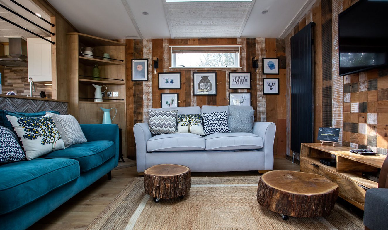 An image of the interior of one of our luxury holiday lodges as part of the May Bank holiday offer. The walls have wood panneling and there's pair of blue and grey two seater sofas.