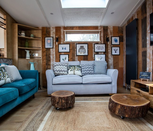 An image of the interior of one of our luxury holiday lodges as part of the May Bank holiday offer. The walls have wood panneling and there's pair of blue and grey two seater sofas.