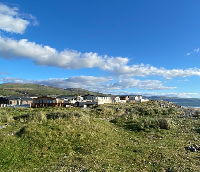 Our Barmouth Bay holiday park. The long beach stretches far into the distance, with greenery leading to the holiday homes. The sea is in the distance.
