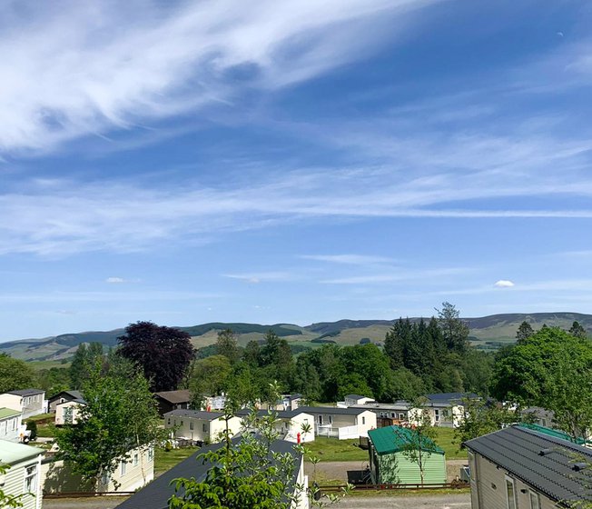 Our Moffat Manor holiday park. There are several luxurious holiday homes onsite, with tall trees and hills in the background.