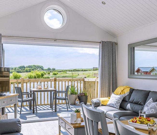 The lounge area of The Meadow Lakeside Lodge at The Bay Filey, which leads out to the decking area overlooking the lake on a sunny day.
