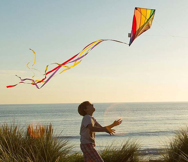 An image of a young boy and his father playing with a kite by the beach on a sunset evening.