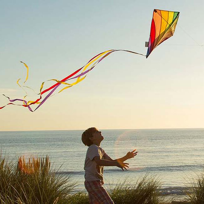 
                An image of a young boy and his father playing with a kite by the beach on a sunset evening.
                