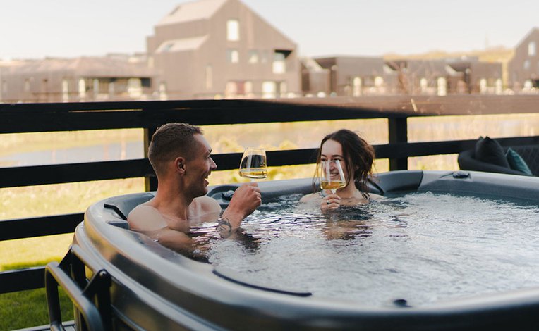 A couple in the hot tub at our stunning Cornish park, Retallack Resort. The male and female are enjoying a glass of wine together.