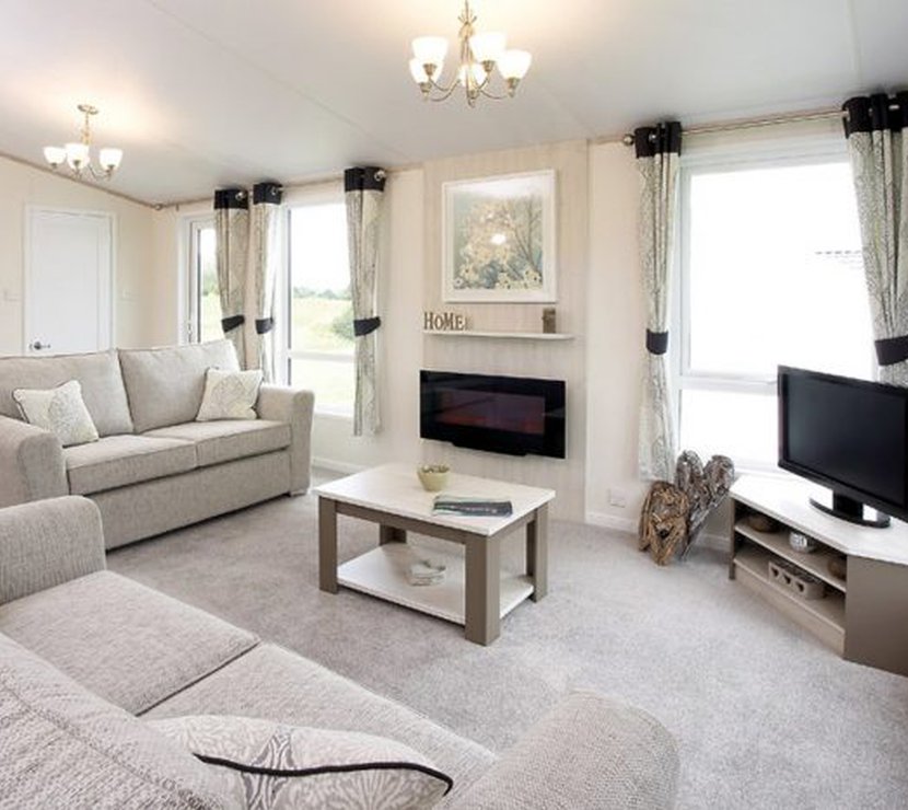 The interior of one of our Luxury holiday lodges. There are two large sofas, a TV, and plenty of space around a coffee table.