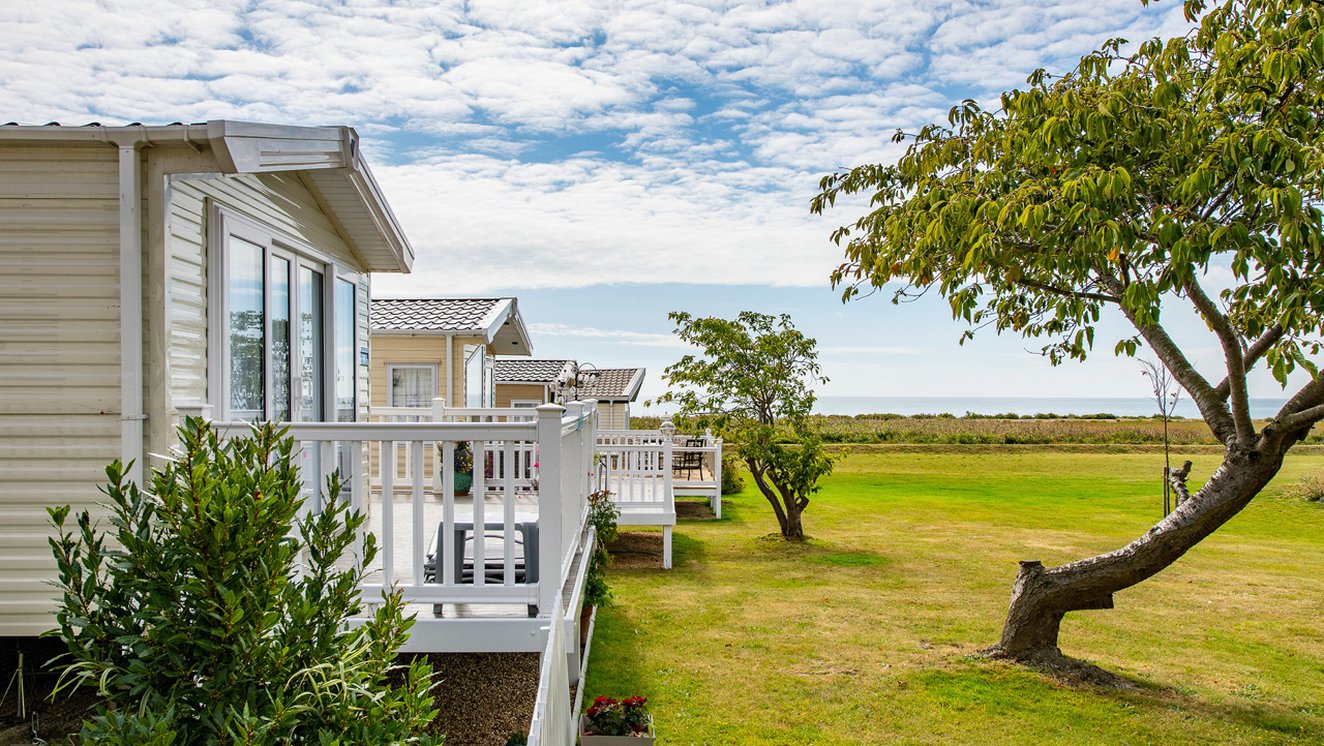 
              A row of caravans at our park in Essex, Mersea Island, with views of the sea in the background.
              