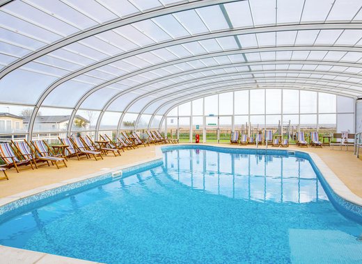 The awesome indoor swimming pool at our holiday park in Essex, Mersea Island. There are multicoloured deck chairs all around the pool.