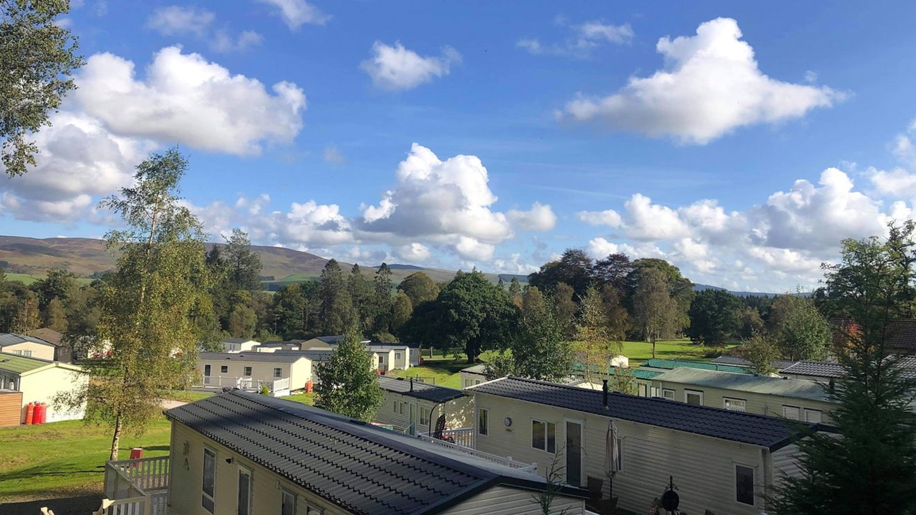 
              An aerial view above the roofs of holiday caravans in Moffat Manor, with hills in the distance.
              
