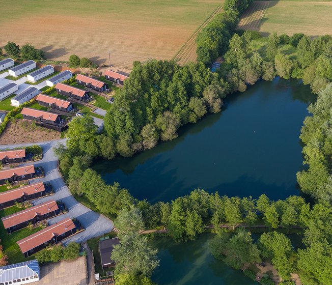 An aerial view of a lake with holiday homes surrounding the lake, with caravans in the distance.