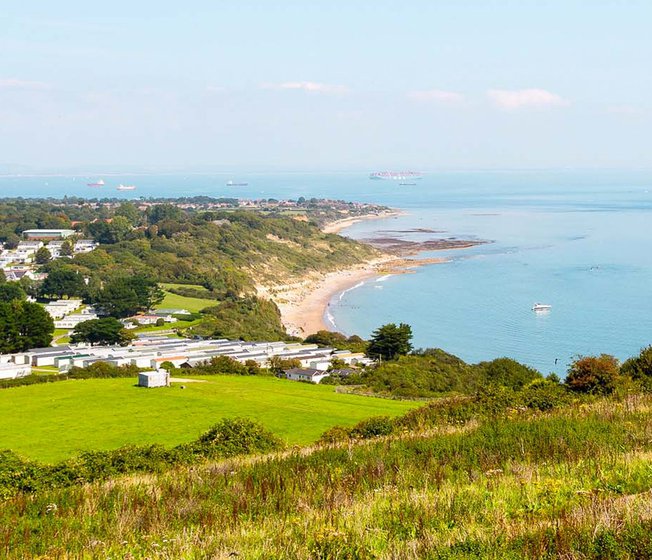 A view of our Whitecliff Bay holiday park. The cliffs are overlooking the sea, with plenty of boats cruising around. The coastline stretches far into the distance.