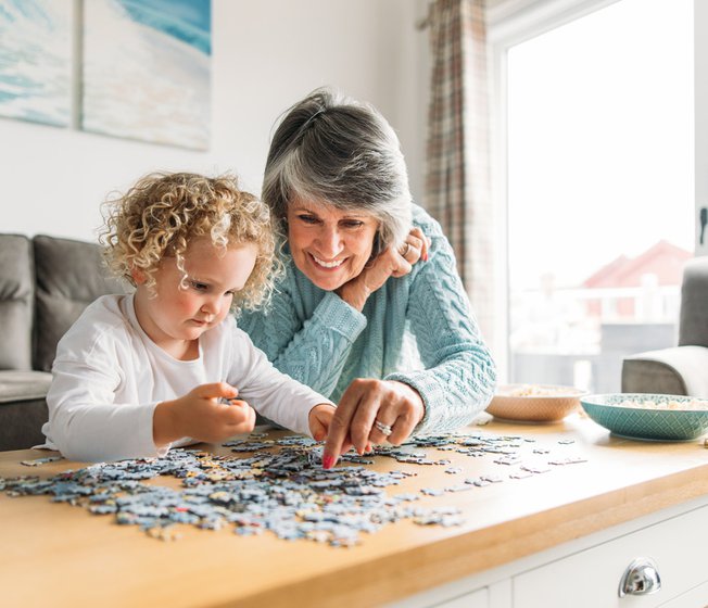 A grandma and granddaughter completing a puzzle together.