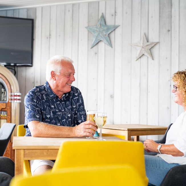 
                A couple enjoying a drink together at The Muddy Duck Clubhouse at our Essex holiday park, Mersea Island.
                