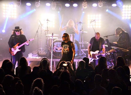 A band of 4 adult men are on stage playing a song with a cheering crowd.