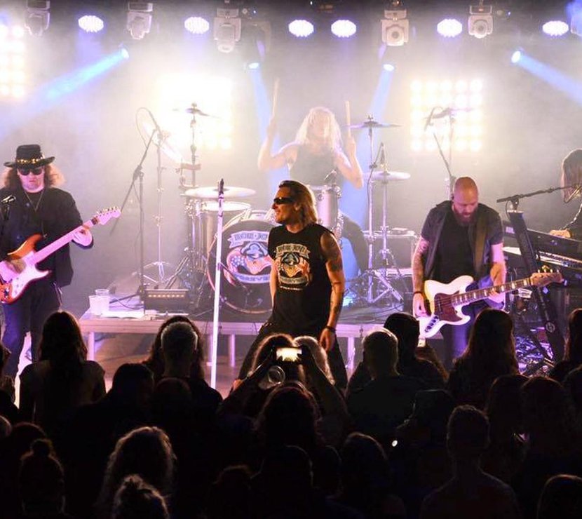 A band of 4 adult men are on stage playing a song with a cheering crowd.