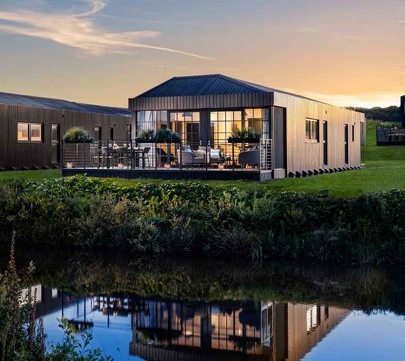 The outside of one of our Retallack holiday barns. The evening sun is shining on the holiday home, which is situated right near a peaceful lake.