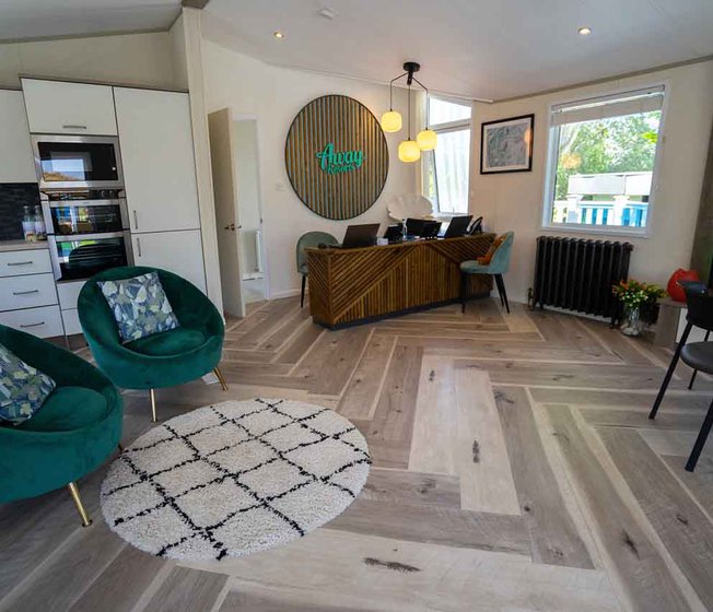 An interior view of inside the Away Resorts Holiday Homes sales office. There is a wooden reception desk, teal blue seats and a wooden sign above the desk saying, "Away Resorts" in blue font.