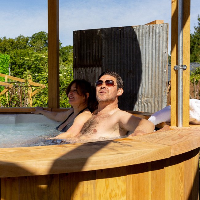 
                A middle-aged couple sitting in a bubbling hot tub under a canopy. On the edge of the hot tub is a bottle of prosecco.
                