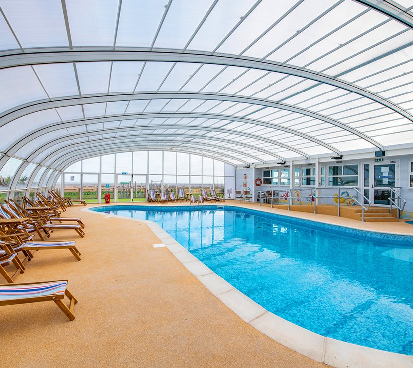 A view of the indoor swimming pool at our Essex holiday park, Mersea Island. Multicoloured deck chairs can be seen around the pool.