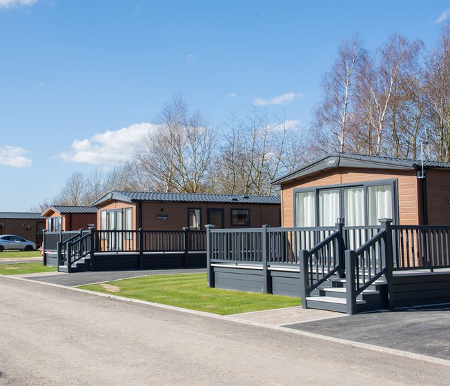 A photo of a row of wooden holiday lodges at our holiday park Appletree, Lincolnshire on a cloudy sunny day.