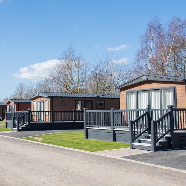 
              A photo of a row of wooden holiday lodges at our holiday park Appletree, Lincolnshire on a cloudy sunny day.
              