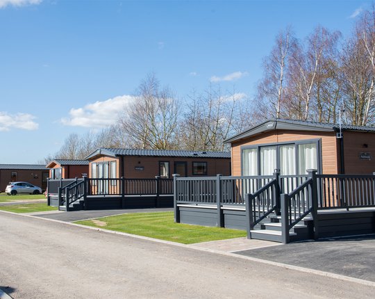 Our amazing lodges at our Appletree holiday park. There are lodges in a row, each with a large porch and double doors.