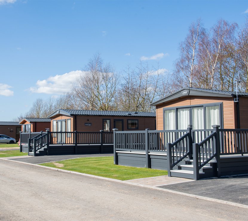 Our amazing lodges at our Appletree holiday park. There are lodges in a row, each with a large porch and double doors.