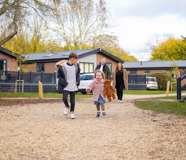 A young family are walking towards the camera on a pebble car park at one of our holiday parks.